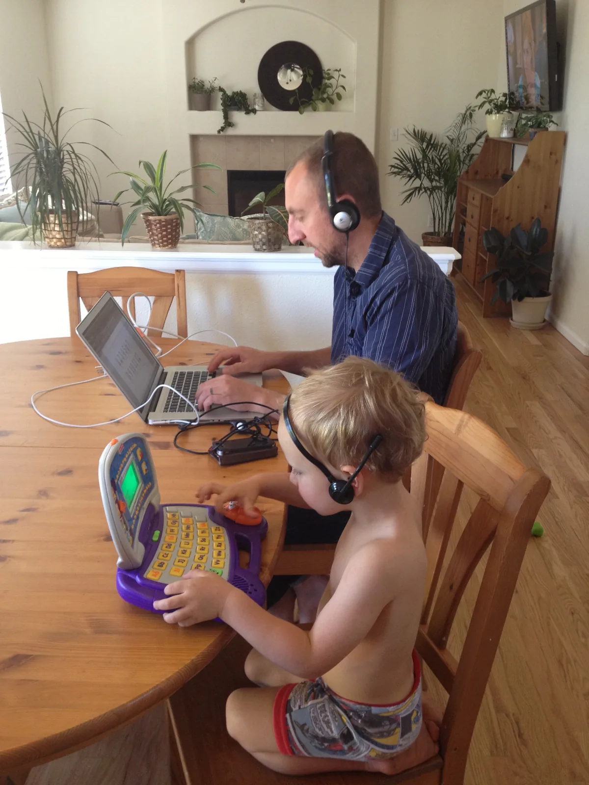 Aaron working at a laptop beside his child using a toy computer
